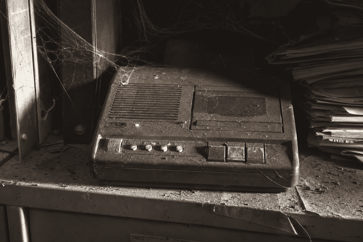 A dusty vintage answering machine with a blinking message light on an office shelf.