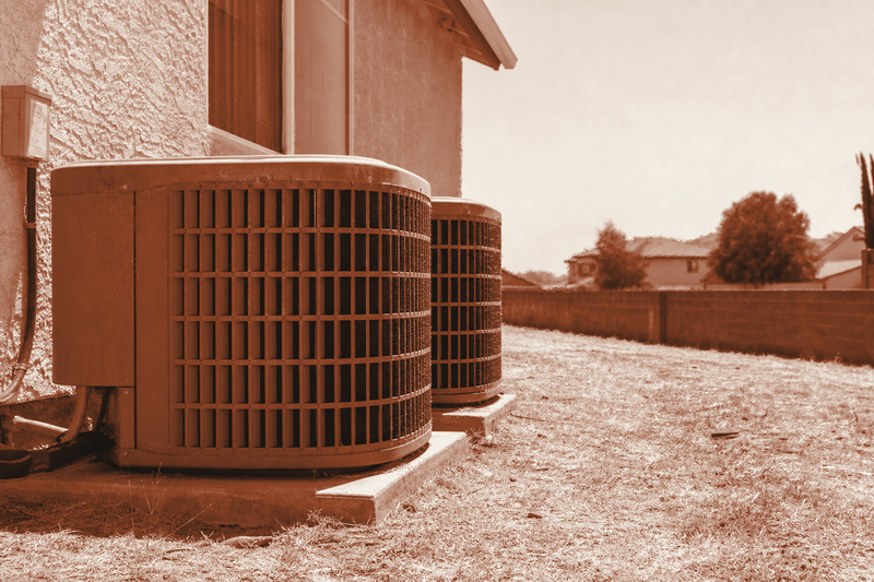 Residential AC condenser units baking in the sun beside a house during a summer heat wave.